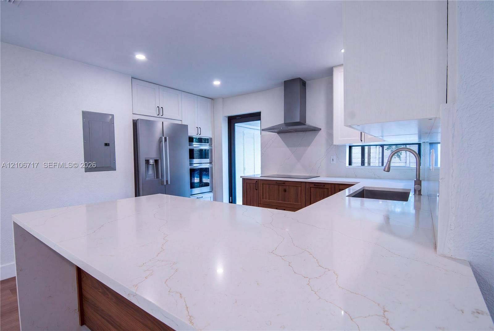 6811 Thomas Street, Hollywood, FL 33024 Kitchen featuring white stone-finish countertops, stainless steel appliances, built-in double wall ovens, wood-finish cabinetry, and a modern stainless steel vent hood