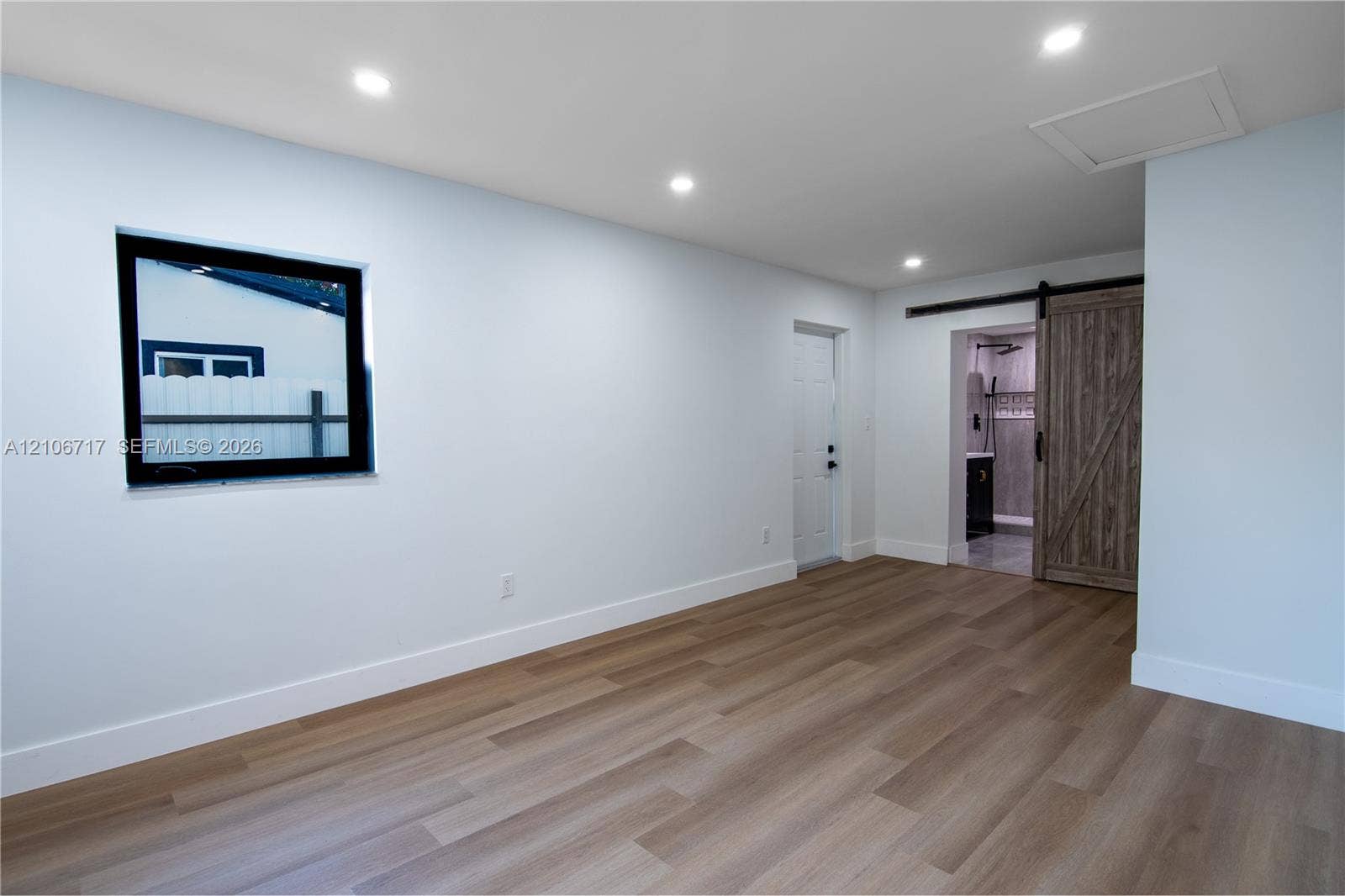 6811 Thomas Street, Hollywood, FL 33024 Neutral interior space featuring wood-finish flooring, recessed lighting, a single-hung window with a dark frame, and a sliding barn-style door