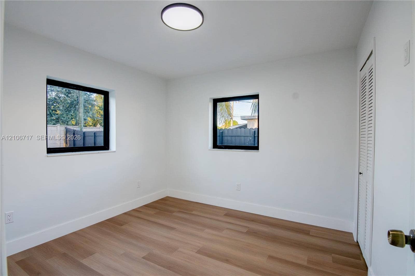 6811 Thomas Street, Hollywood, FL 33024 Interior space featuring wood-finish flooring, two dual-pane windows with black frames, a flush-mount ceiling light fixture, and a louvered bi-fold closet door