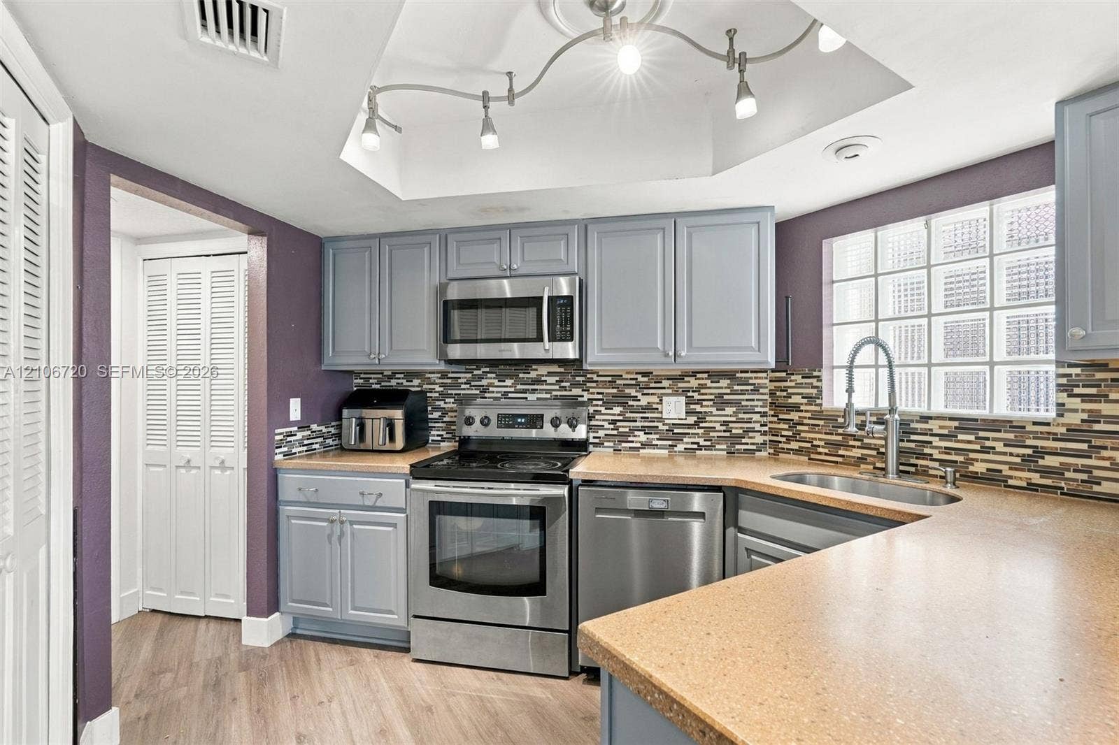 152 Weybridge Circle, #C, Royal Palm Beach, FL 33411 Kitchen featuring shaker-style cabinetry, stainless steel appliances, multi-toned mosaic tile backsplash, solid-surface countertops, and a glass block window