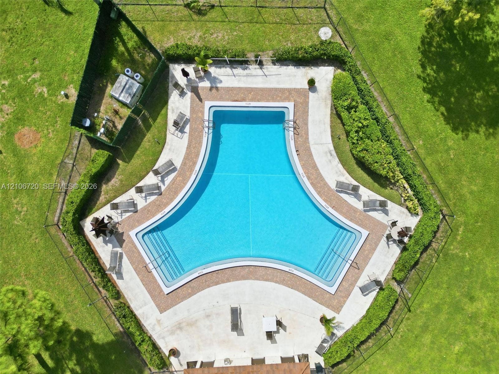 152 Weybridge Circle, #C, Royal Palm Beach, FL 33411 T-shaped pool with integrated stairs, surrounded by a paved deck, enclosed by perimeter fencing and landscaped hedges within a grass lawn