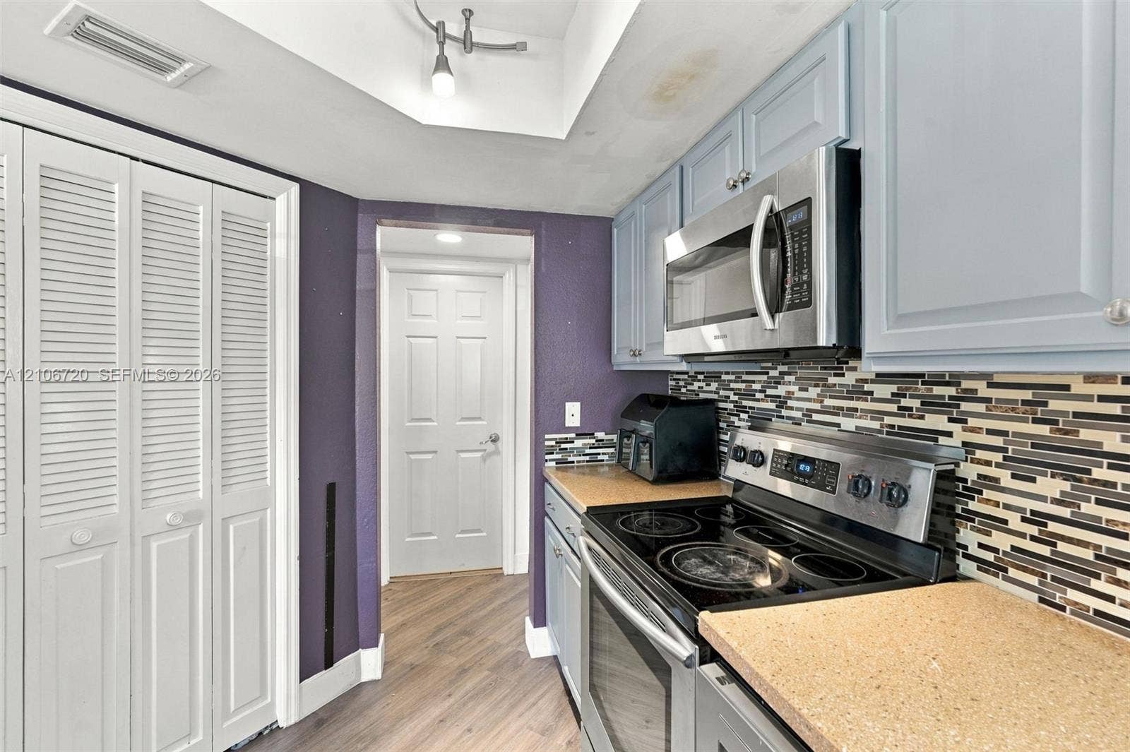 152 Weybridge Circle, #C, Royal Palm Beach, FL 33411 Kitchen featuring light blue cabinetry, stainless steel microwave, glass-top electric range, multi-toned mosaic tile backsplash, and wood-finish flooring