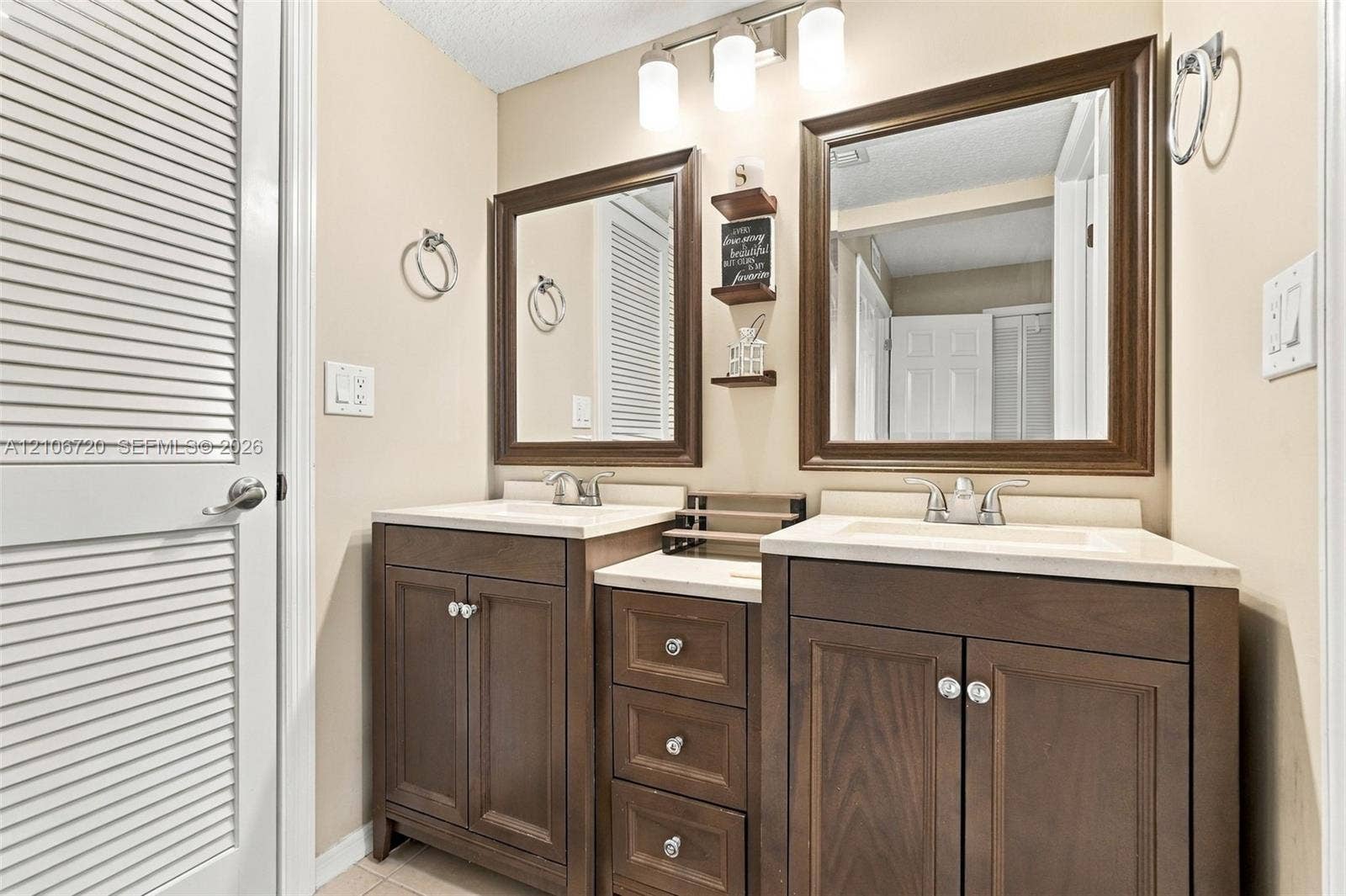 152 Weybridge Circle, #C, Royal Palm Beach, FL 33411 Double vanity featuring wood cabinetry, stone-composite countertops with integrated sinks, three-light overhead fixture, and dual framed mirrors