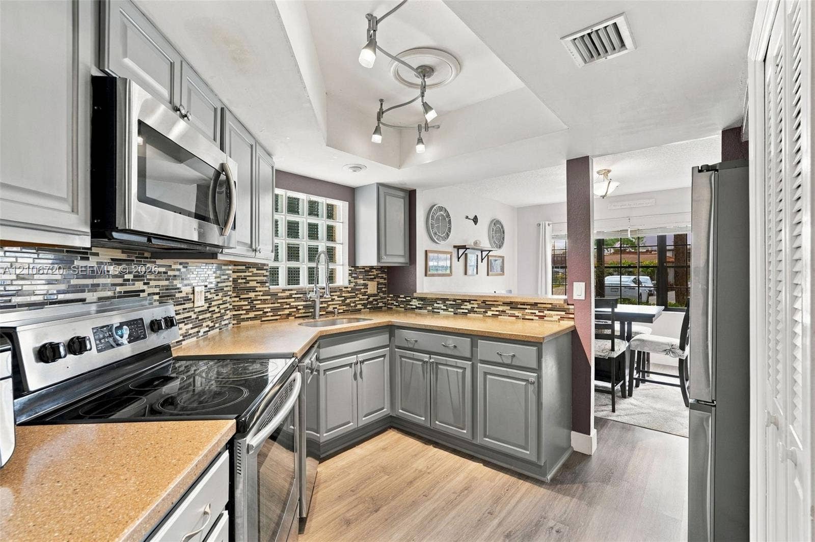152 Weybridge Circle, #C, Royal Palm Beach, FL 33411 Kitchen featuring gray cabinetry, composite countertops, multi-toned tile backsplash, stainless steel appliances, and wood-finish flooring
