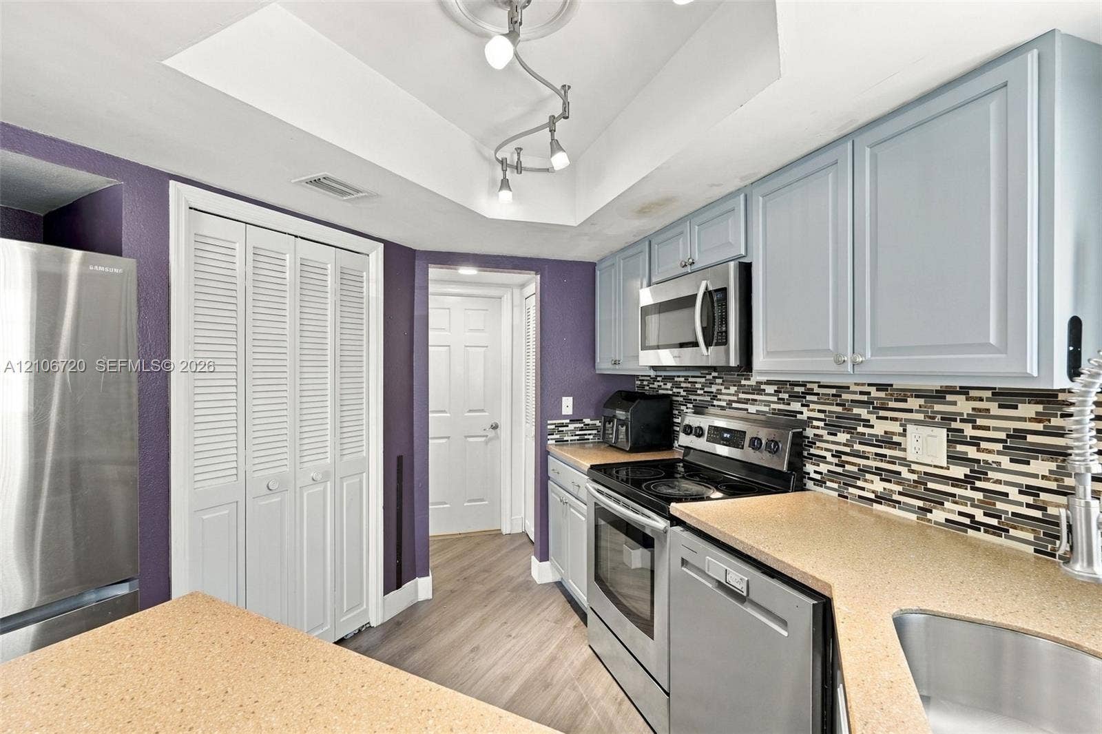 152 Weybridge Circle, #C, Royal Palm Beach, FL 33411 Kitchen featuring stainless steel appliances, multi-toned tile backsplash, solid-surface countertops, light-finish cabinetry, and wood-finish flooring
