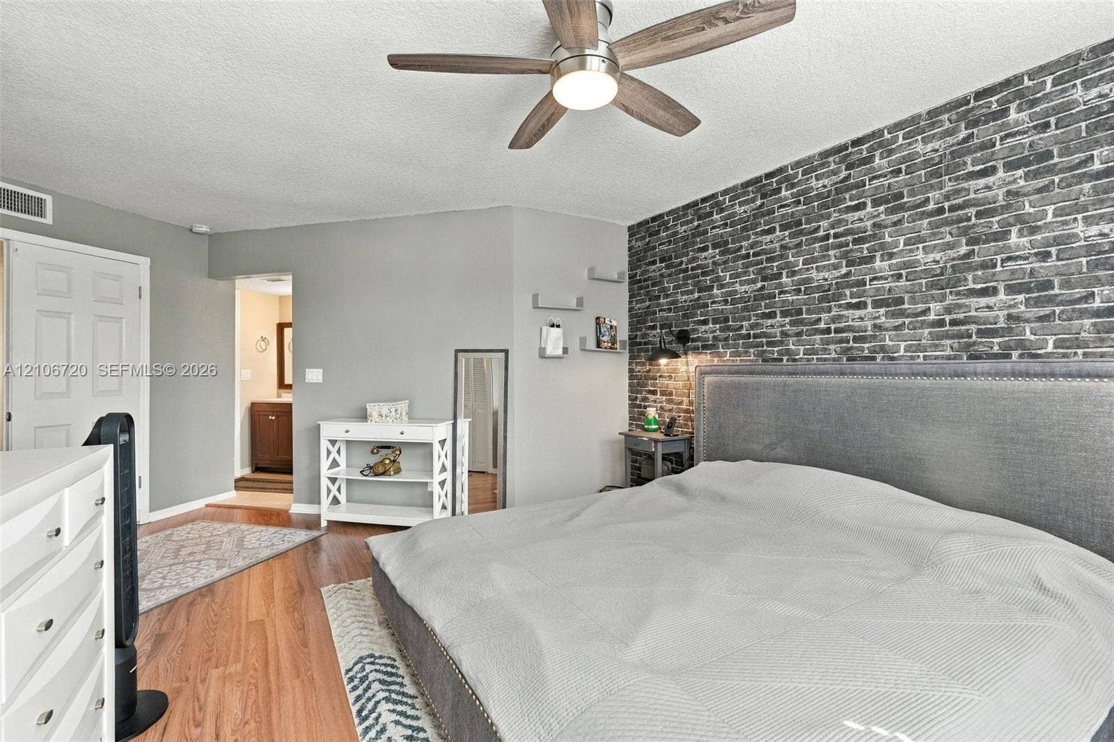 152 Weybridge Circle, #C, Royal Palm Beach, FL 33411 Bedroom featuring an exposed brick accent wall, wood-finish flooring, and a ceiling fan with integrated lighting