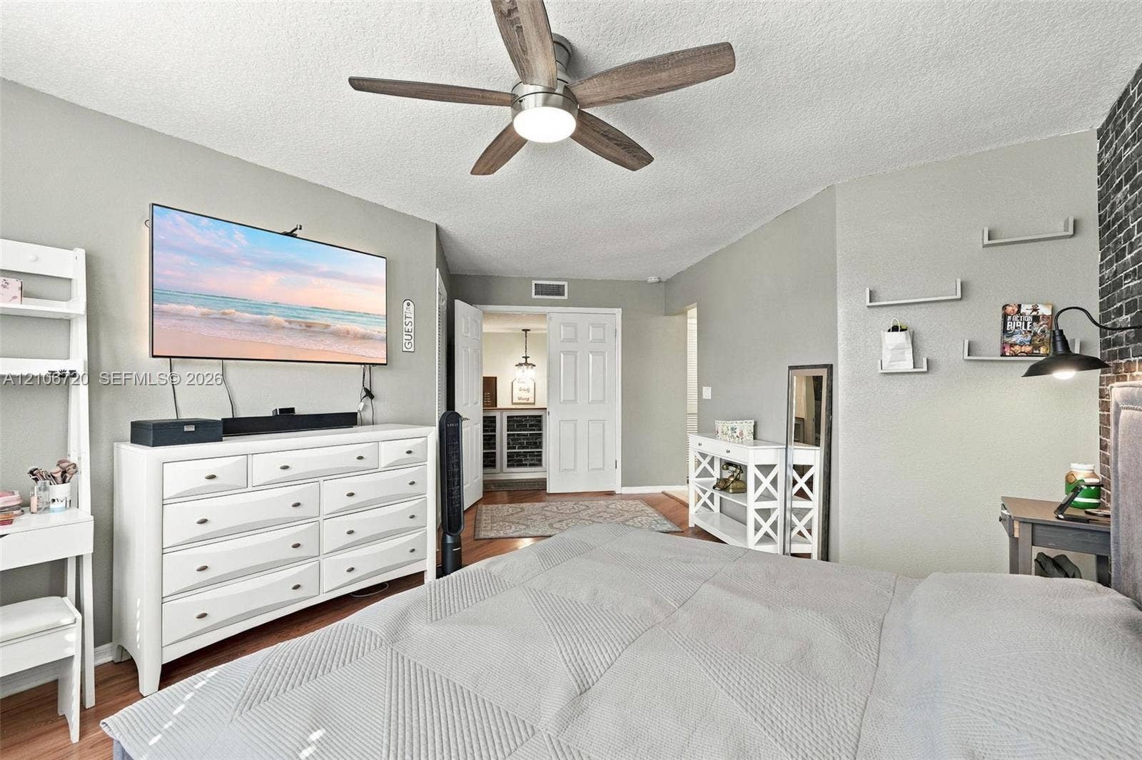 152 Weybridge Circle, #C, Royal Palm Beach, FL 33411 Neutral-toned bedroom featuring a dark brick-veneer accent wall, multi-shelf wall-mounted organizers, and a central ceiling fan with integrated lighting