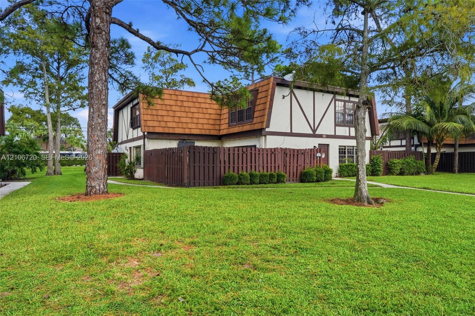 152 Weybridge Circle, #C, Royal Palm Beach, FL 33411 Two-story residence featuring a mansard roof, exterior timber framing, integrated wood privacy fencing, and mature pine trees on the grounds