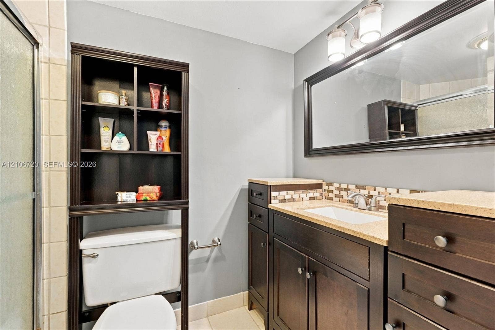 152 Weybridge Circle, #C, Royal Palm Beach, FL 33411 Dark wood vanity with a stone-finish countertop, integrated undermount sink, multi-tile backsplash, and expansive framed wall mirror with overhead multi-light fixture