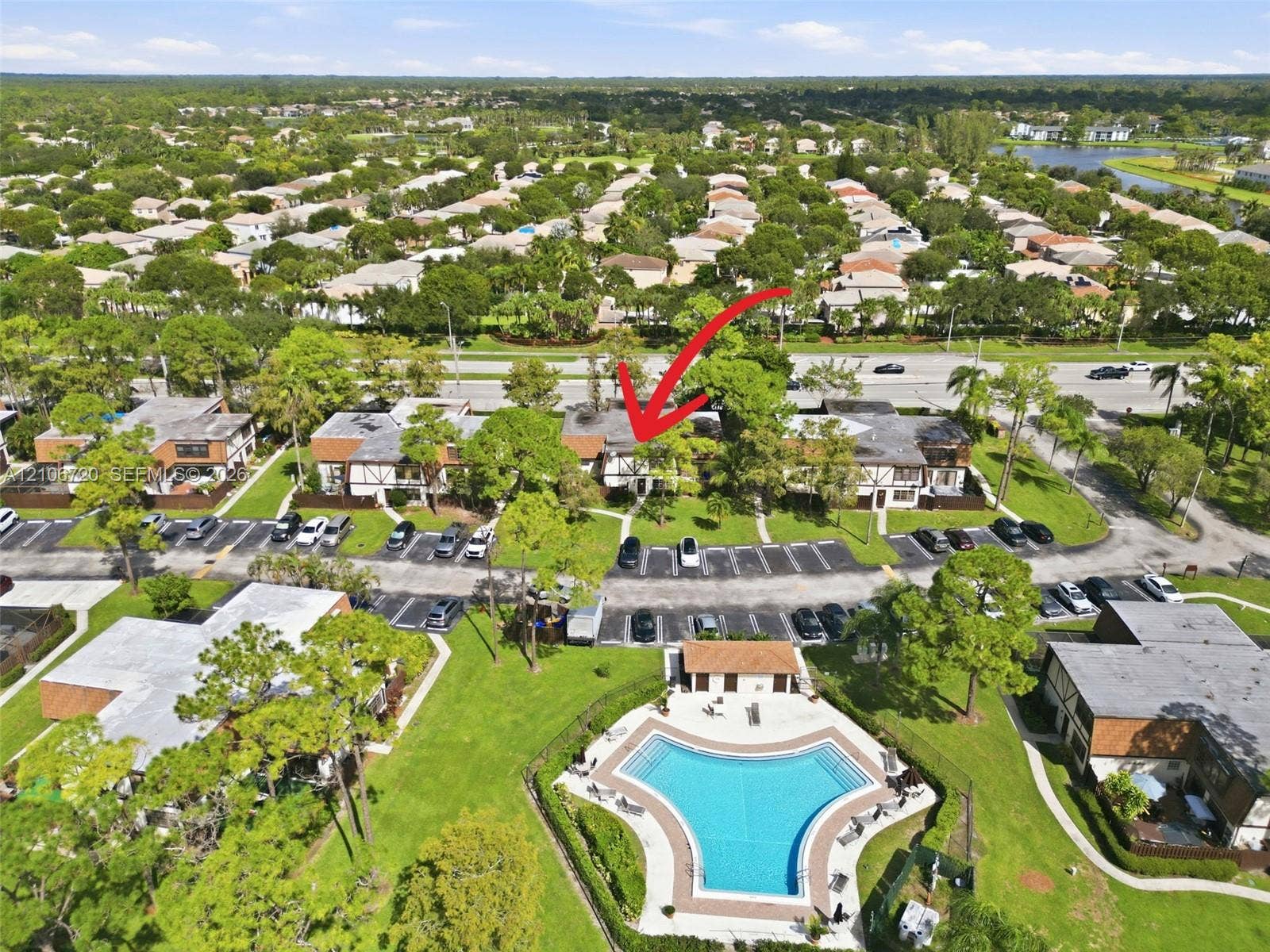 152 Weybridge Circle, #C, Royal Palm Beach, FL 33411 Aerial view of the residential complex featuring multi-unit dwellings, paved surface parking, extensive surrounding greenery, and a community swimming pool