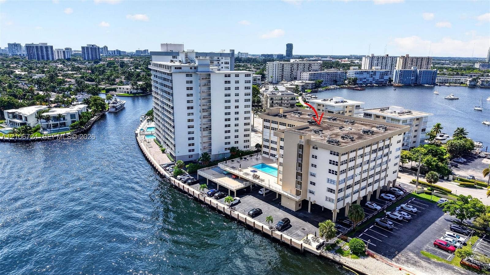 Aerial perspective of waterfront mid-rise building featuring a swimming pool, covered parking, and direct maritime waterway access