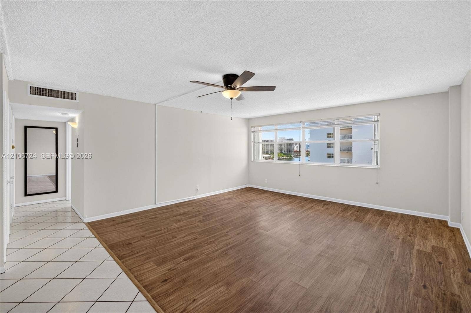 111 Golden Isles Drive, #G12, Hallandale Beach, FL 33009 Open-concept living space featuring wood-finish flooring, white tile entryway, multi-pane windows, and a central ceiling fan with integrated lighting