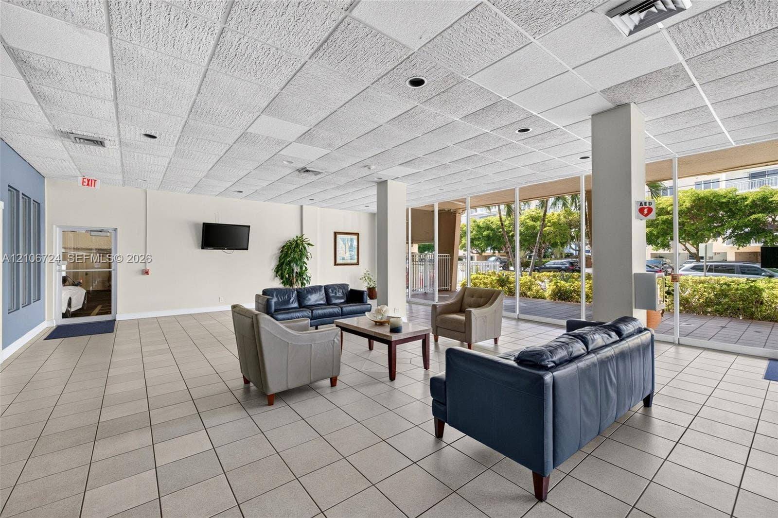 111 Golden Isles Drive, #G12, Hallandale Beach, FL 33009 Open-concept common area featuring large floor-to-ceiling windows, uniform tile flooring, recessed lighting, and a neutral color palette