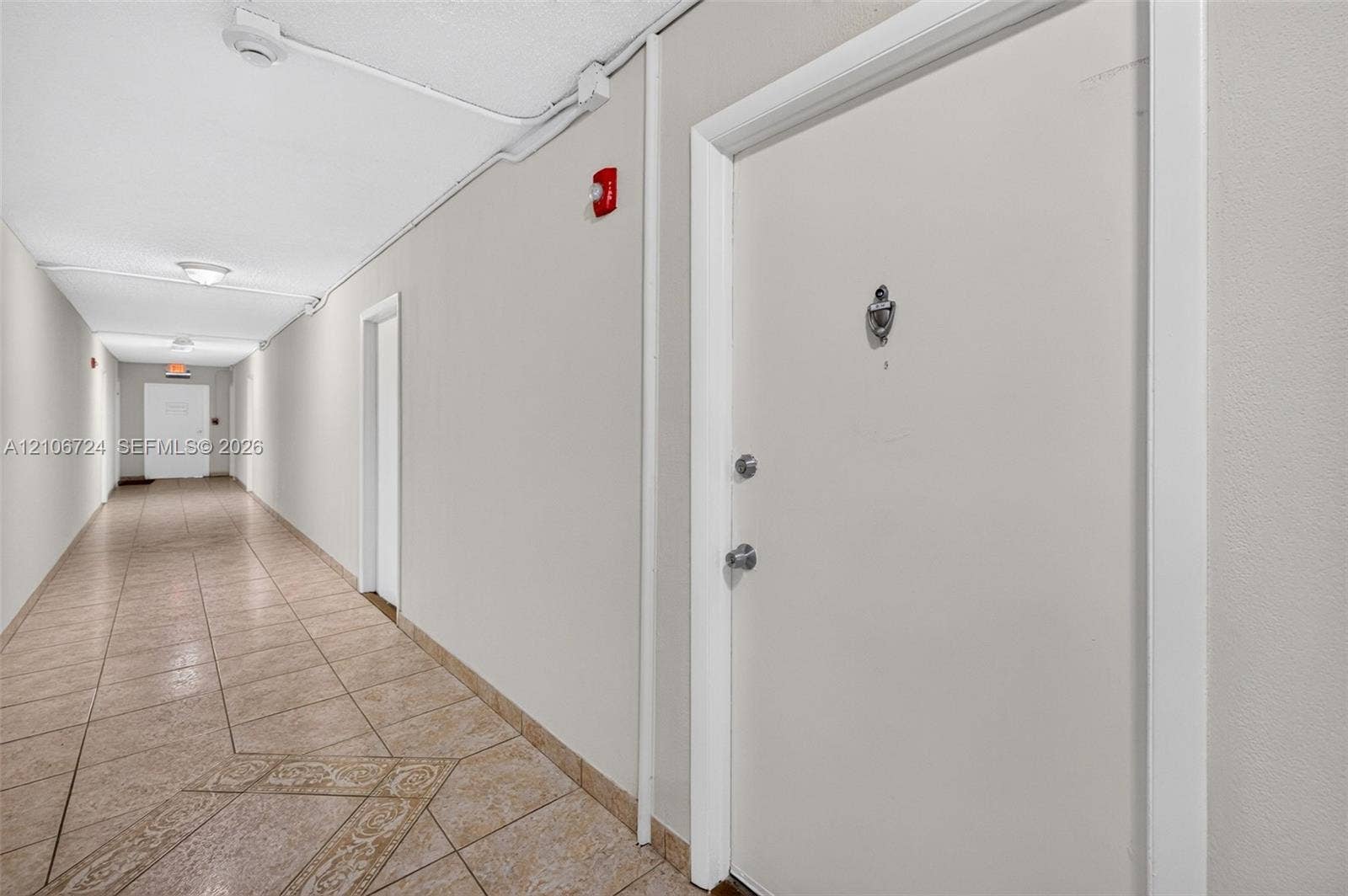 Interior corridor featuring tile flooring with decorative inlay, solid-core doors, and recessed ceiling lighting
