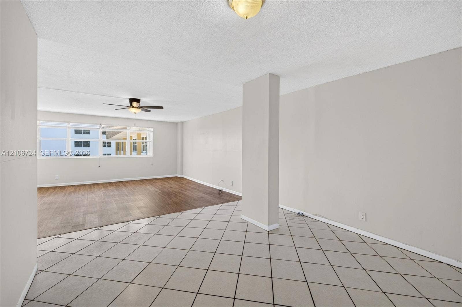 111 Golden Isles Drive, #G12, Hallandale Beach, FL 33009 Open-concept interior featuring large-format diagonal tile flooring, wood-finish flooring, a ceiling fan with integrated lighting, and a prominent structural pillar
