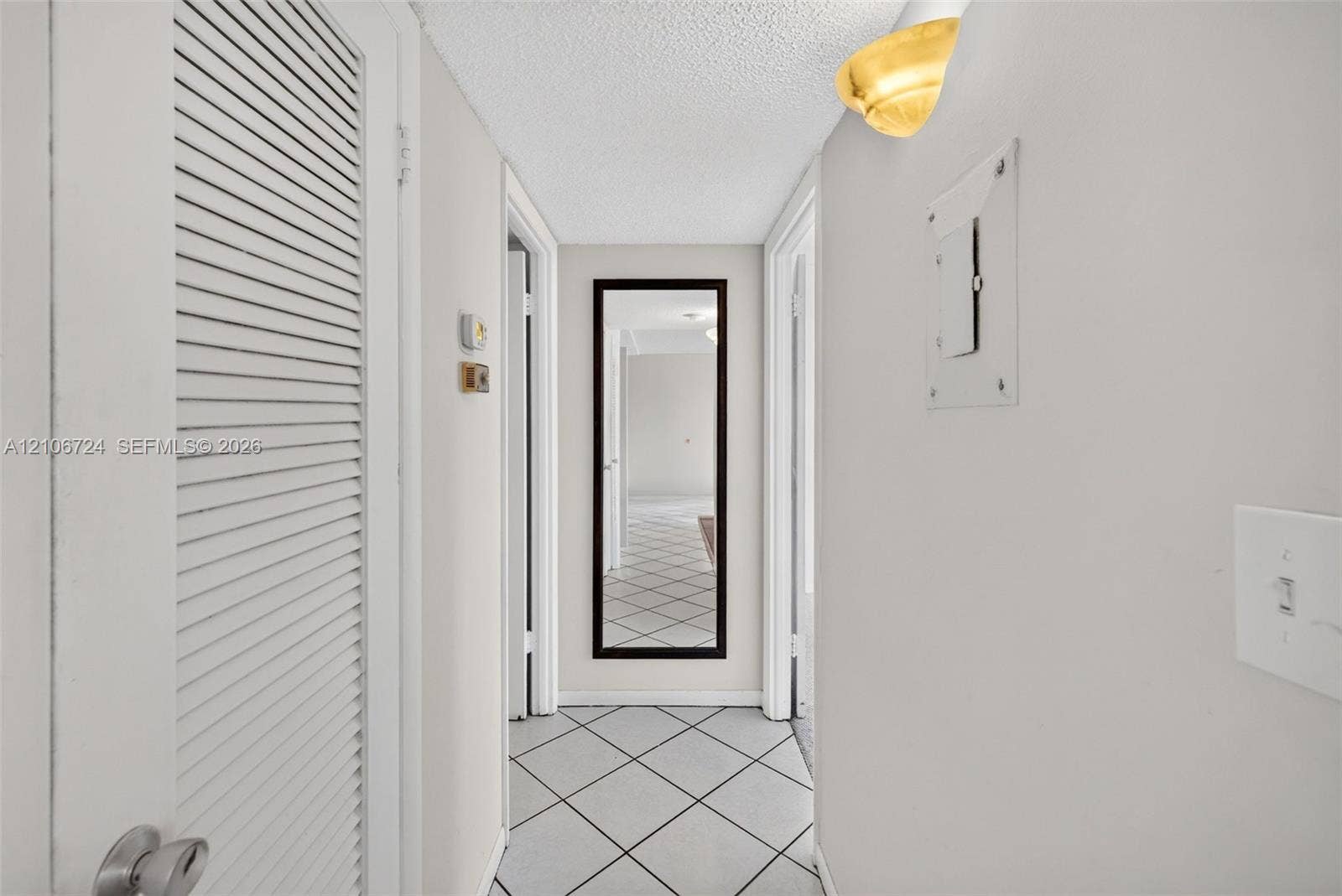 111 Golden Isles Drive, #G12, Hallandale Beach, FL 33009 Hallway featuring diamond-patterned tile flooring, louvered closet door, and half-dome wall-mounted light fixture