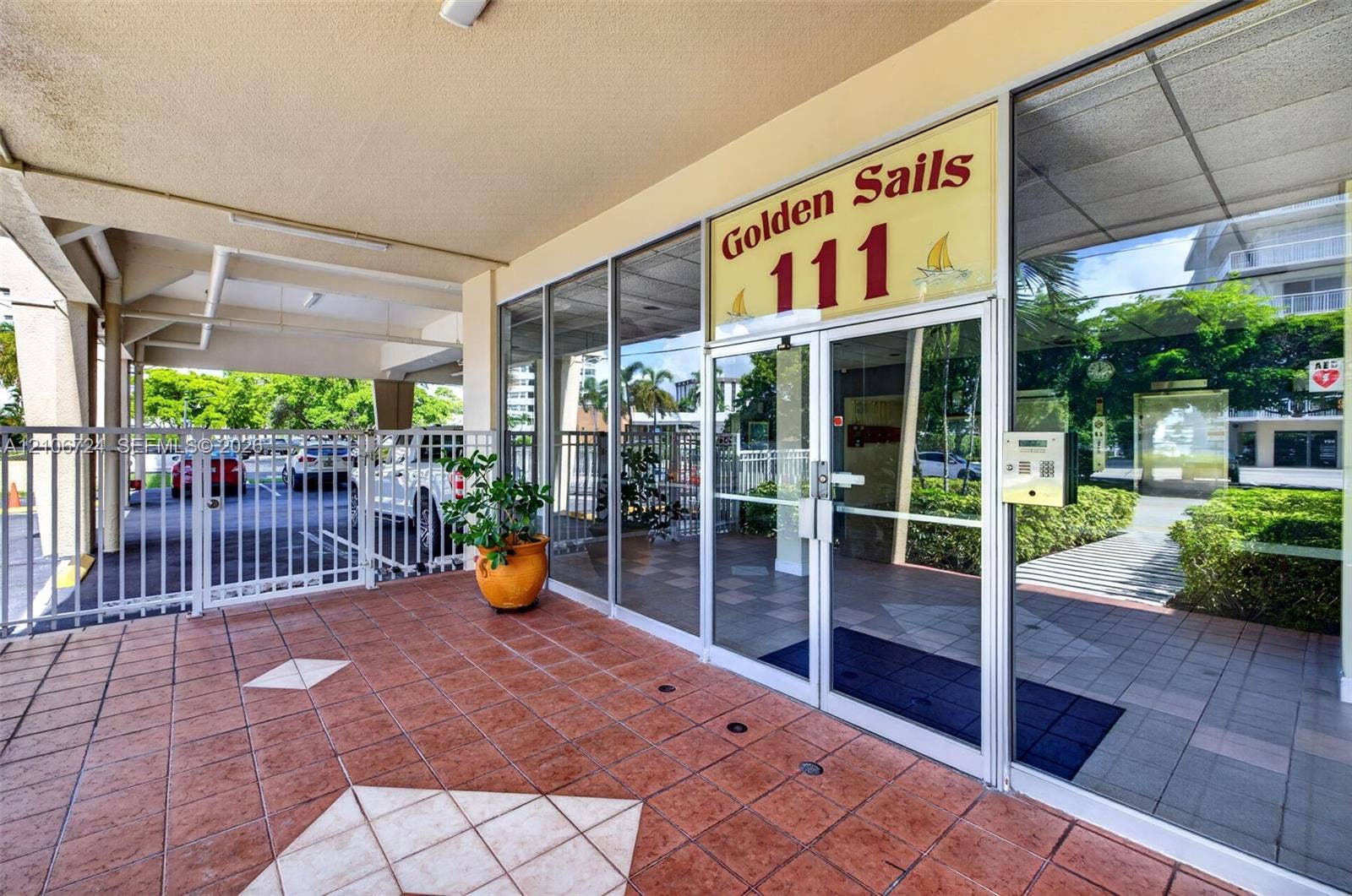 111 Golden Isles Drive, #G12, Hallandale Beach, FL 33009 Covered entryway featuring terra cotta tile flooring, expansive floor-to-ceiling glass windows, secured metal gate access, and built-in intercom system