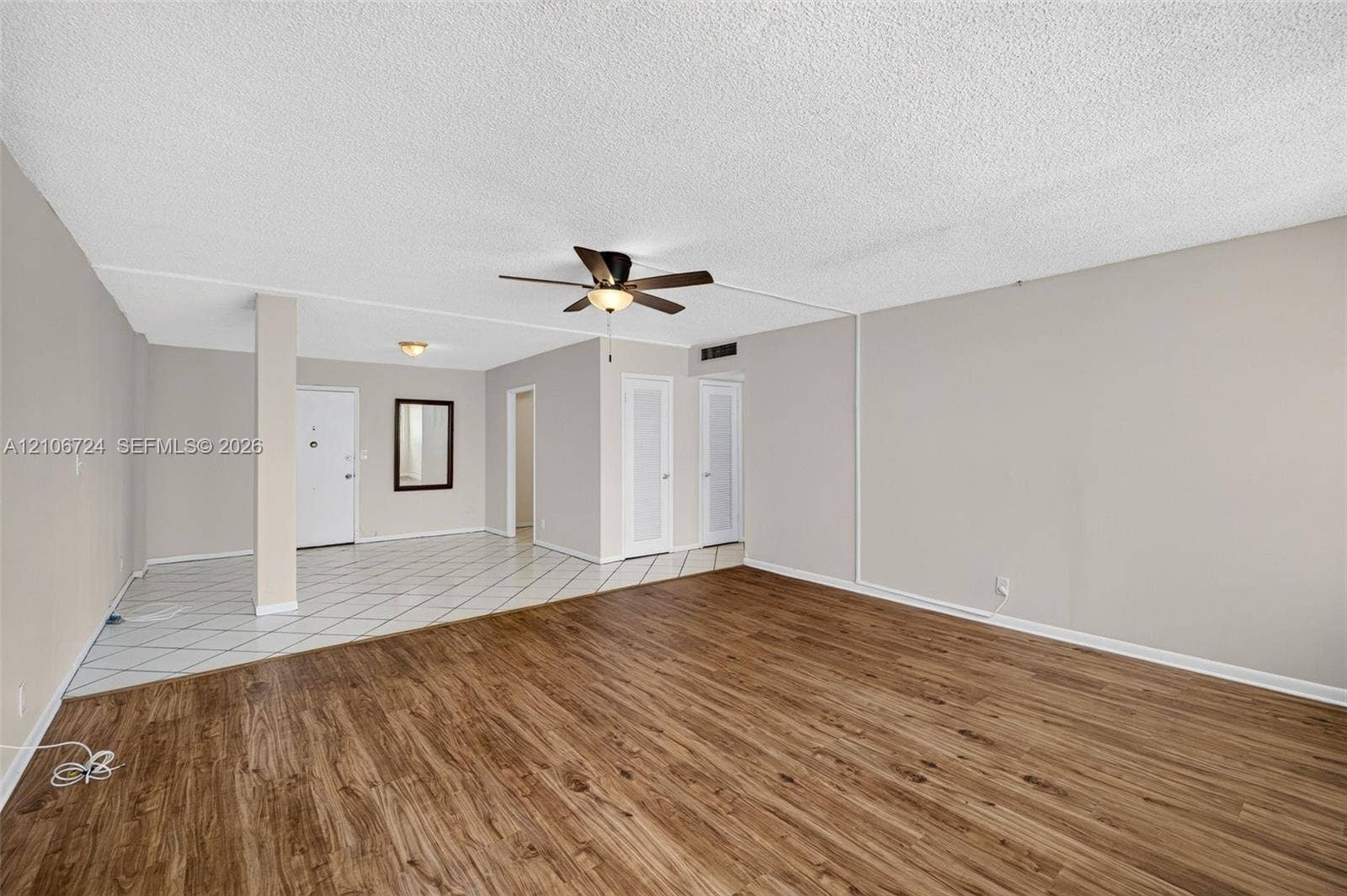 111 Golden Isles Drive, #G12, Hallandale Beach, FL 33009 Open-concept interior featuring wood-finish flooring, ceramic tile flooring, a central structural support pillar, a ceiling fan with integrated lighting, and dual closet doors