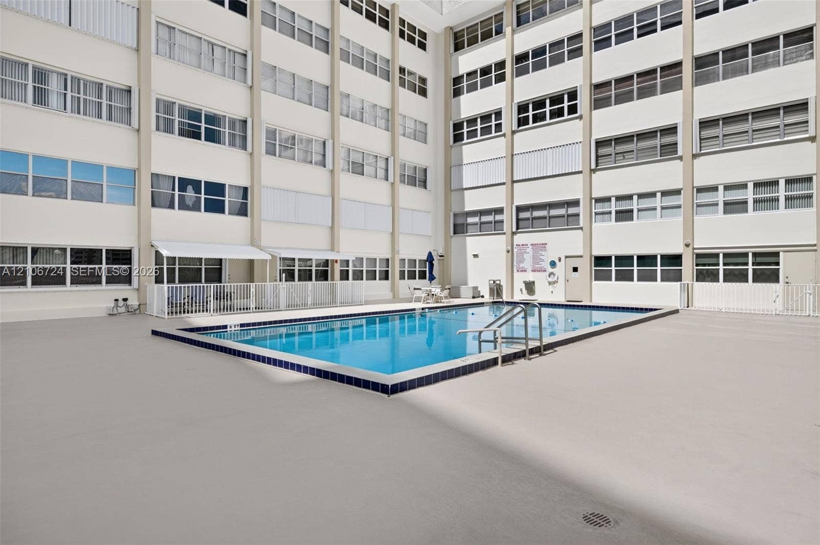 111 Golden Isles Drive, #G12, Hallandale Beach, FL 33009 Rectangular swimming pool with tiled coping and integrated metal handrails, set within a spacious concrete deck surrounded by multi-story residential architecture