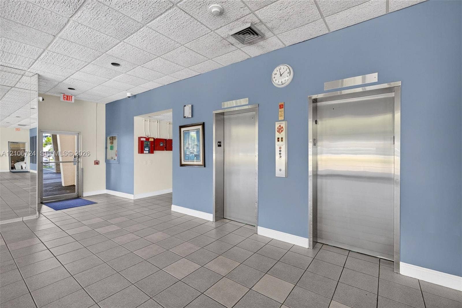 111 Golden Isles Drive, #G12, Hallandale Beach, FL 33009 Lobby area featuring dual stainless steel elevators, ceramic tile flooring, and mirrored wall paneling