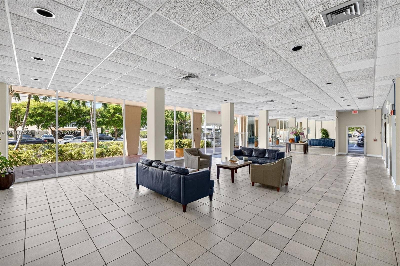 111 Golden Isles Drive, #G12, Hallandale Beach, FL 33009 Open-concept interior featuring floor-to-ceiling glass panel walls, square ceramic tile flooring, recessed lighting, and a drop-grid ceiling