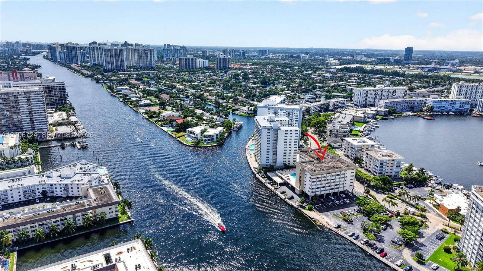 111 Golden Isles Drive, #G12, Hallandale Beach, FL 33009 Aerial perspective of a waterfront mid-rise building featuring a swimming pool, asphalt parking area, and direct canal access