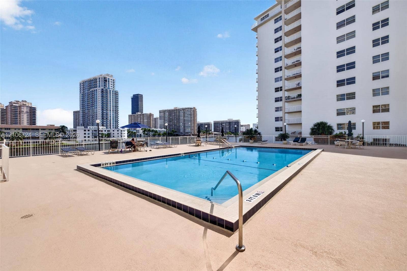 111 Golden Isles Drive, #G12, Hallandale Beach, FL 33009 Rectangular outdoor swimming pool featuring a tiled waterline, metal handrails, and a surrounding paved deck