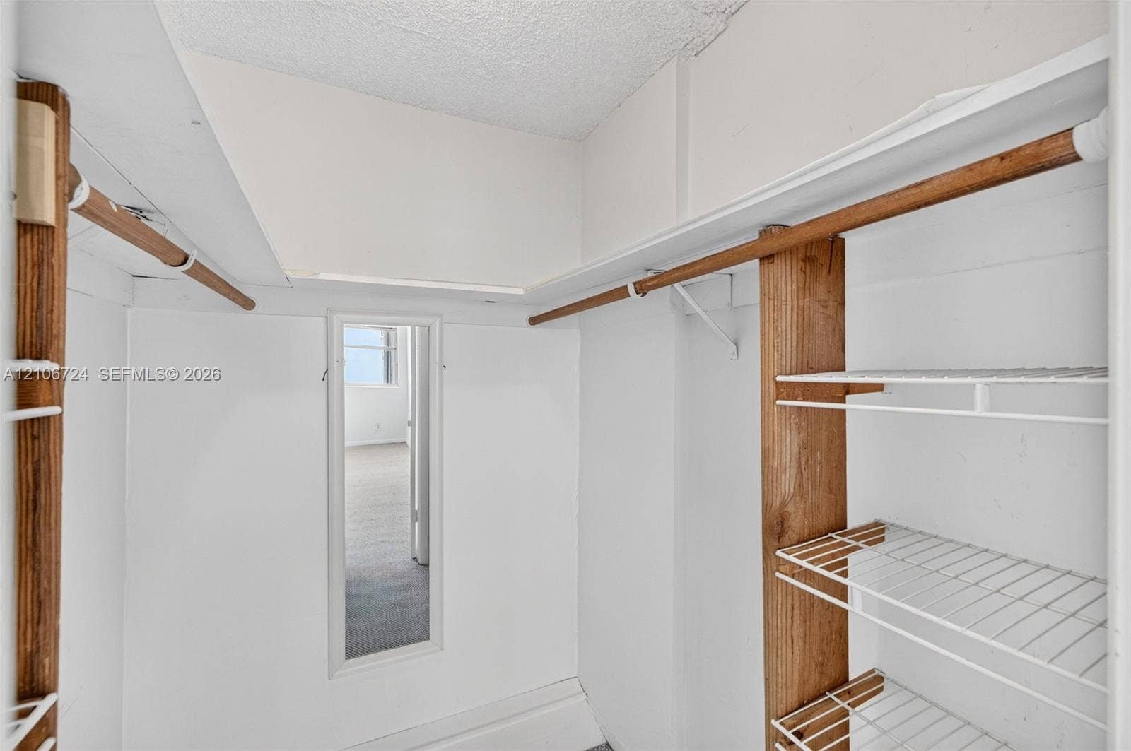 111 Golden Isles Drive, #G12, Hallandale Beach, FL 33009 Storage closet featuring wood-finish support beams, integrated wire shelving, full-length door mirror, and hanging rods
