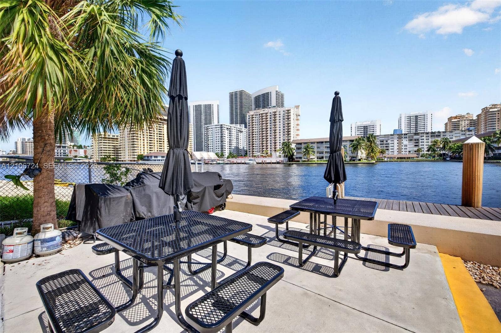 111 Golden Isles Drive, #G12, Hallandale Beach, FL 33009 Waterfront patio area featuring concrete hardscaping, a fixed wooden piling, and a chain-link perimeter fence