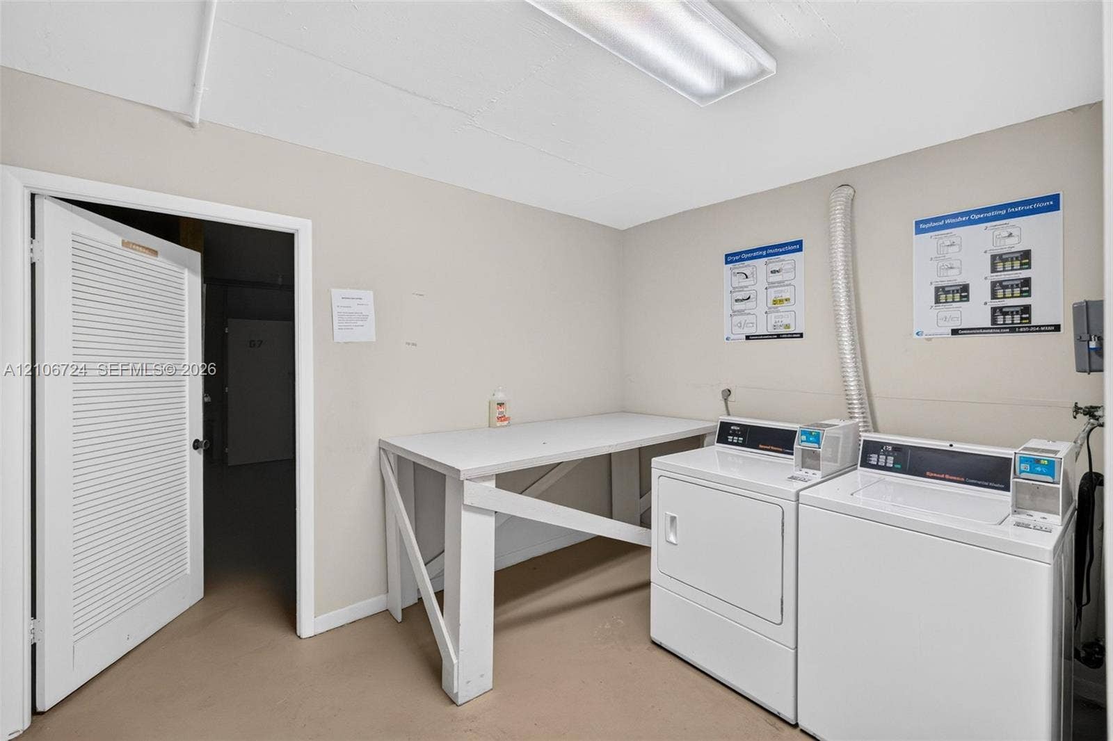 111 Golden Isles Drive, #G12, Hallandale Beach, FL 33009 Utility room featuring built-in white folding table, louvered door, and overhead fluorescent lighting