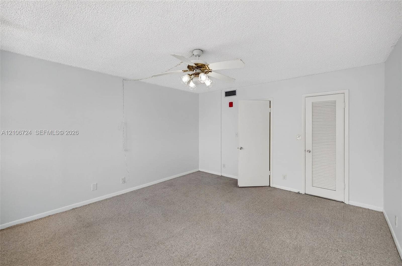 111 Golden Isles Drive, #G12, Hallandale Beach, FL 33009 Interior space featuring neutral wall tones, carpeted flooring, a ceiling fan with integrated lighting, and a louvered door