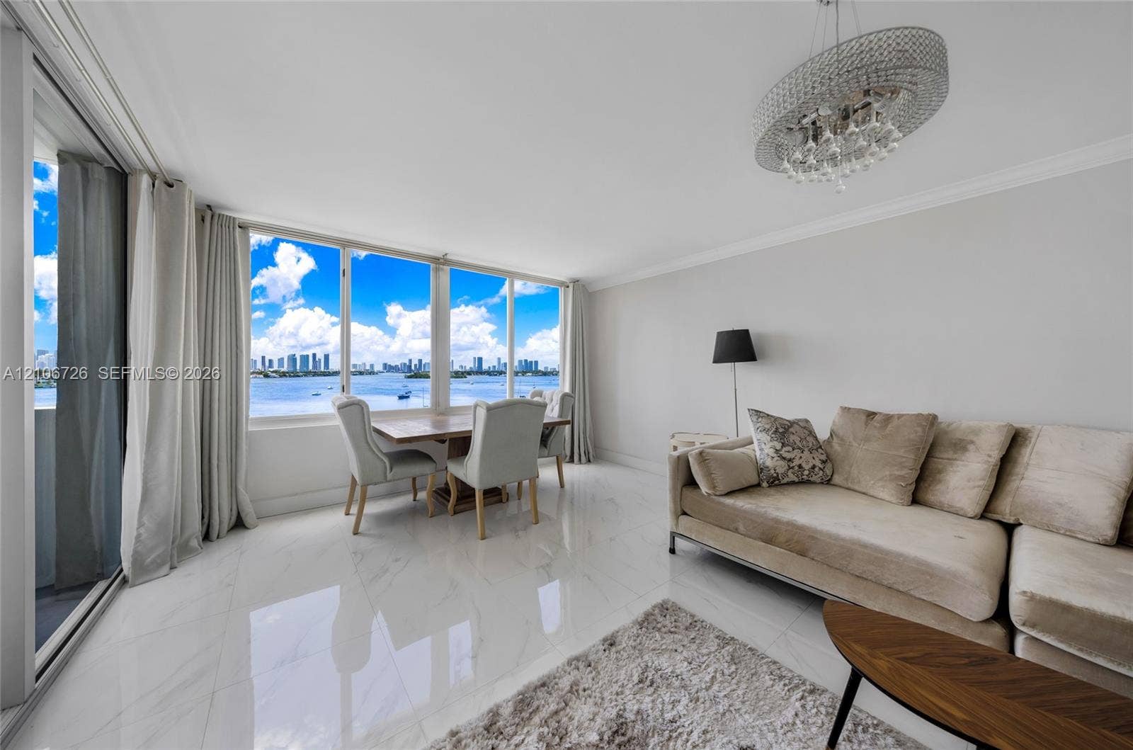 1200 West Avenue, #606, Miami Beach, Miami Beach, FL 33139 Expansive windows featuring water and city skyline scenery, floor-to-ceiling sliding glass doors, polished stone-finish tile flooring, and a crystal-accented chandelier
