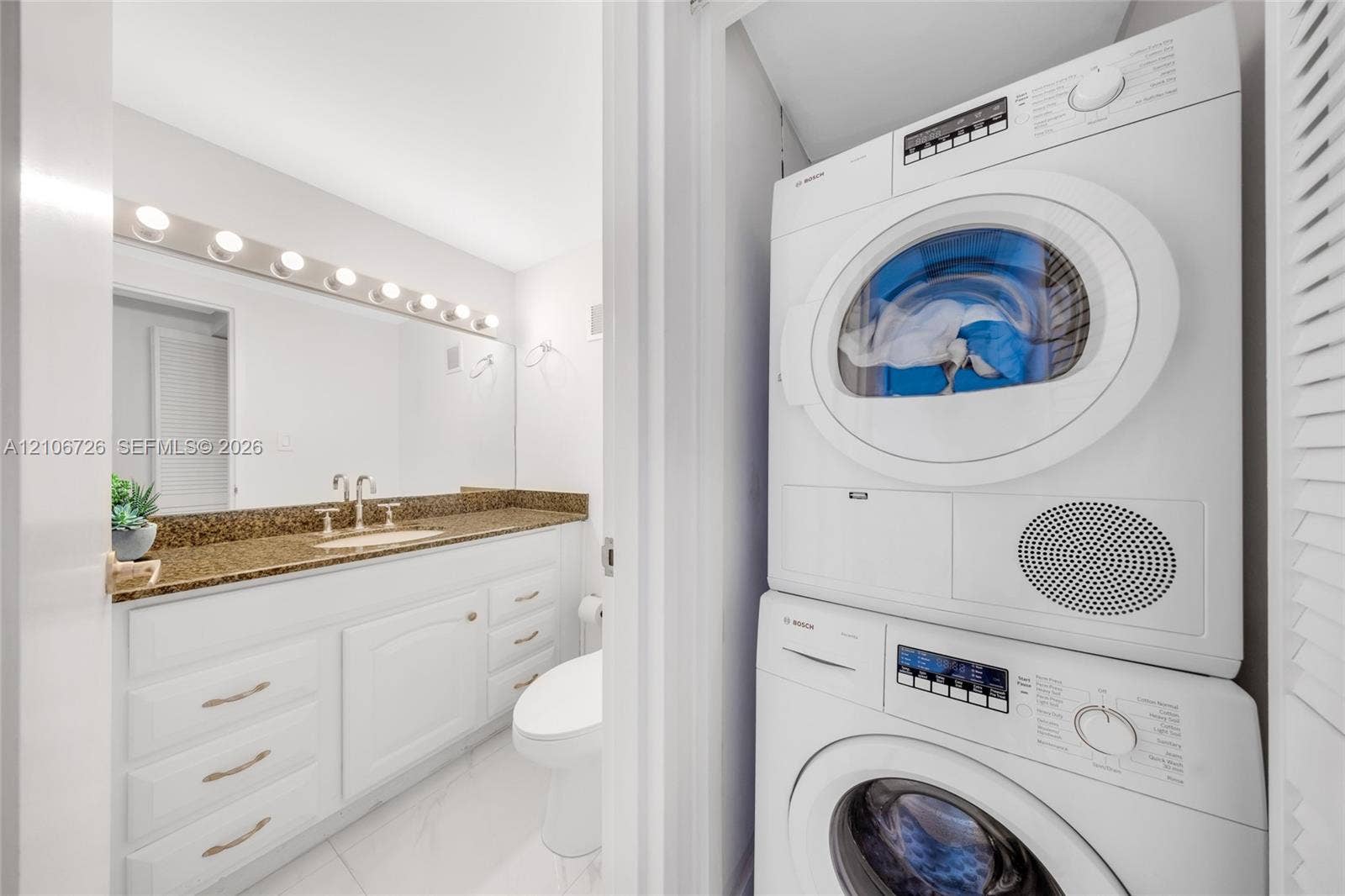 1200 West Avenue, #606, Miami Beach, Miami Beach, FL 33139 Bathroom featuring white cabinetry, stone-finish countertop, full-width mirror with integrated lighting, and stacked front-load laundry appliances
