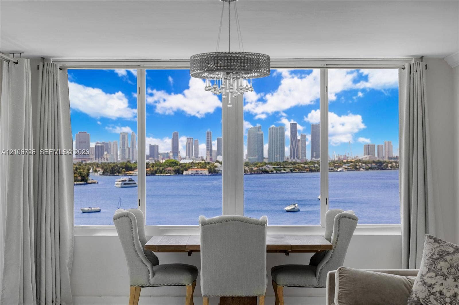 1200 West Avenue, #606, Miami Beach, Miami Beach, FL 33139 Floor-to-ceiling windows featuring panoramic water and city skyline scenery, complemented by a contemporary circular crystal drum chandelier