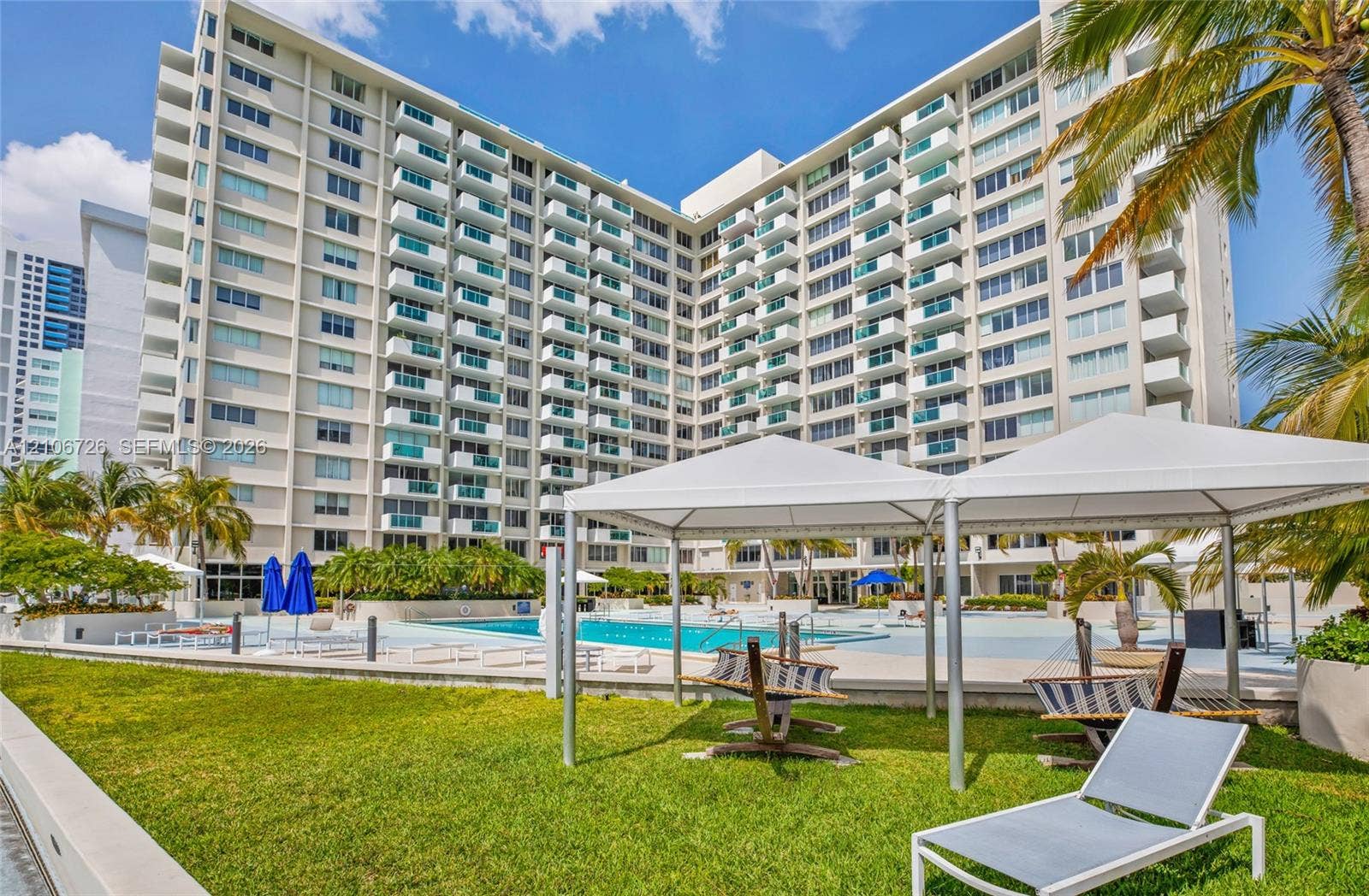 1200 West Avenue, #606, Miami Beach, Miami Beach, FL 33139 Mid-rise residential building featuring private balconies, expansive swimming pool, landscaped lawn, and white structural canopy pavilions