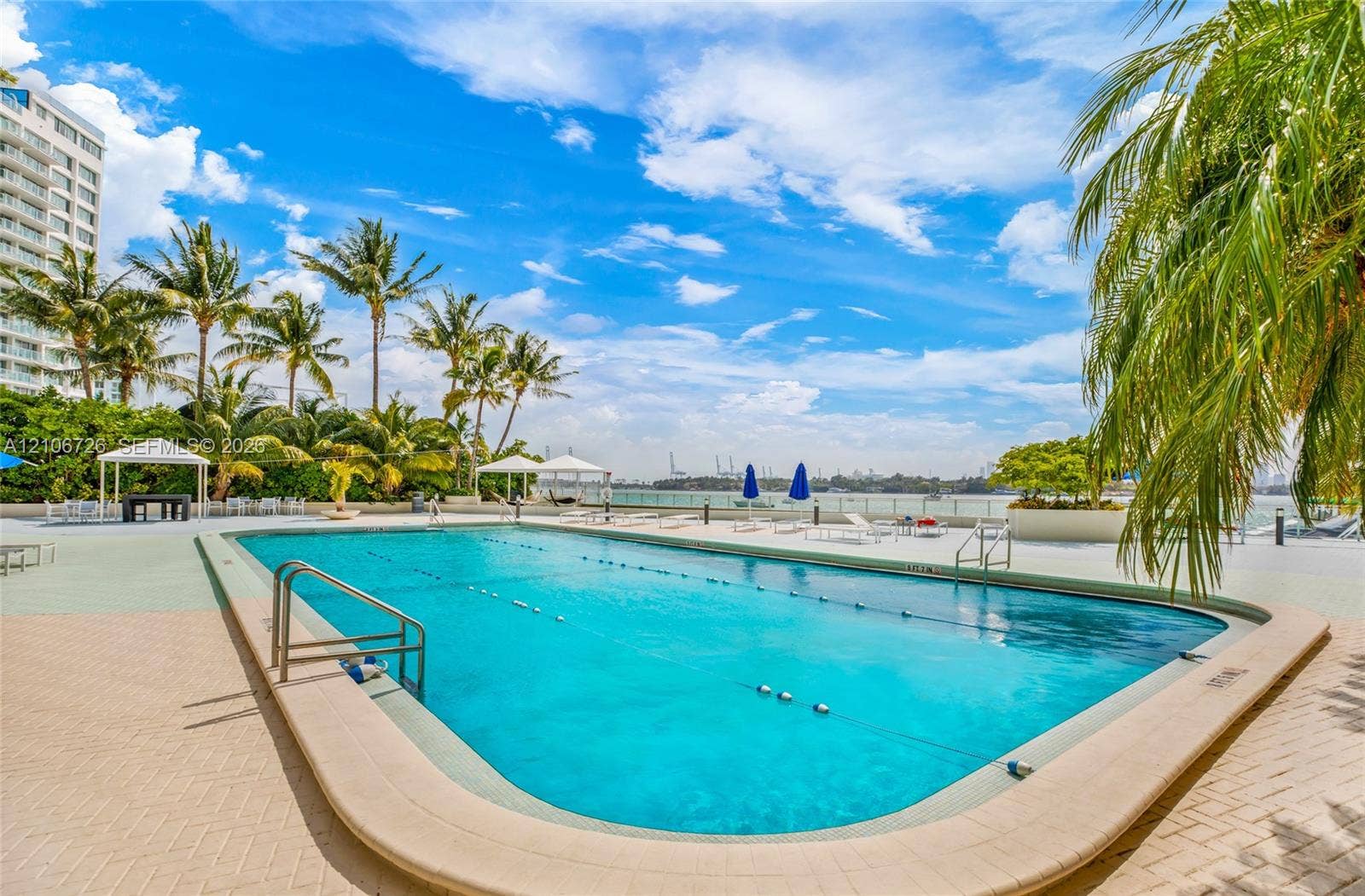 1200 West Avenue, #606, Miami Beach, Miami Beach, FL 33139 Rectangular swimming pool featuring a brick-paver deck, metal handrails, and a perimeter landscape of mature palm trees