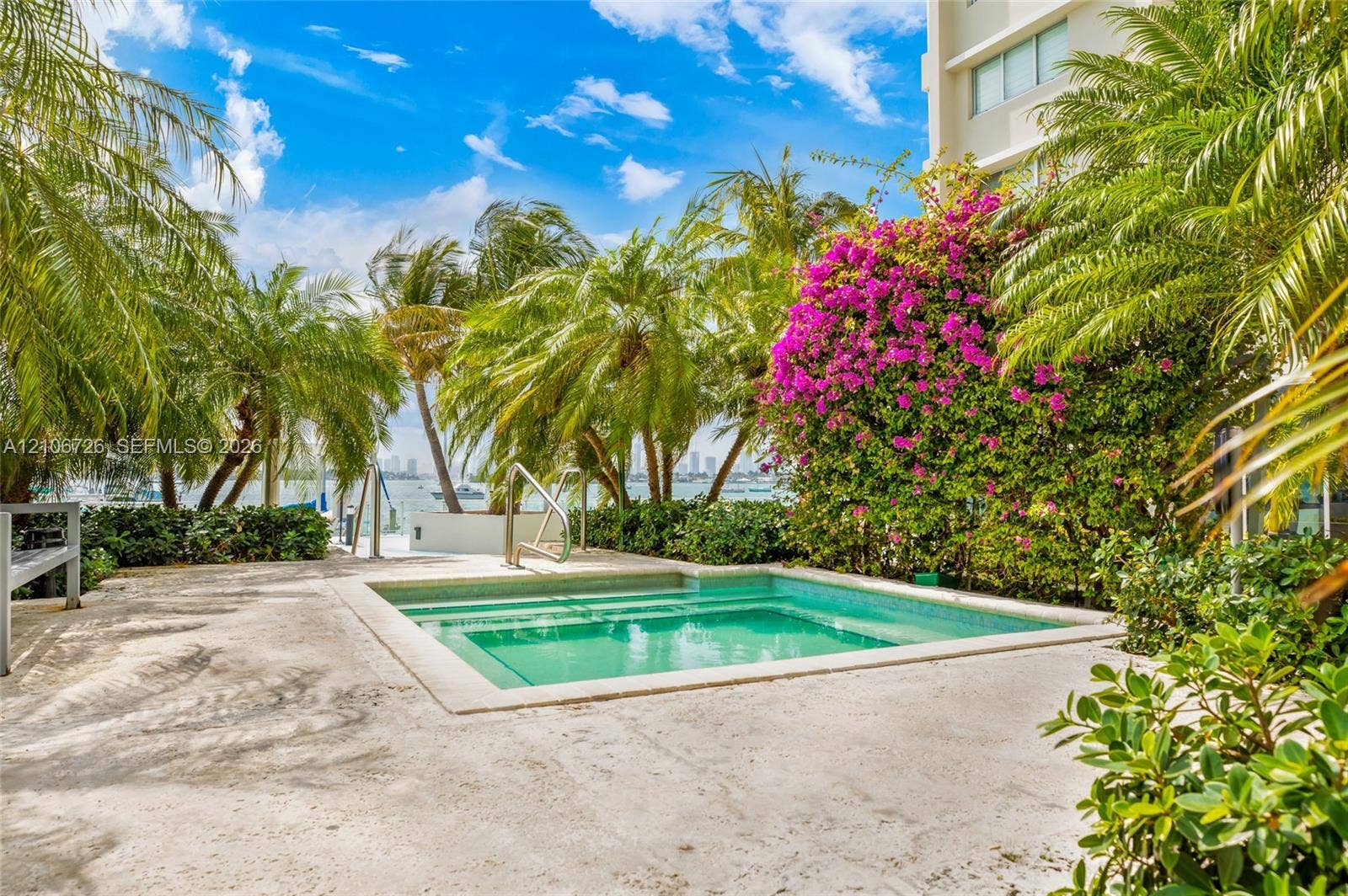 1200 West Avenue, #606, Miami Beach, Miami Beach, FL 33139 In-ground swimming pool featuring a concrete deck, built-in steps, and metal handrail, surrounded by mature palm trees and flowering shrubbery