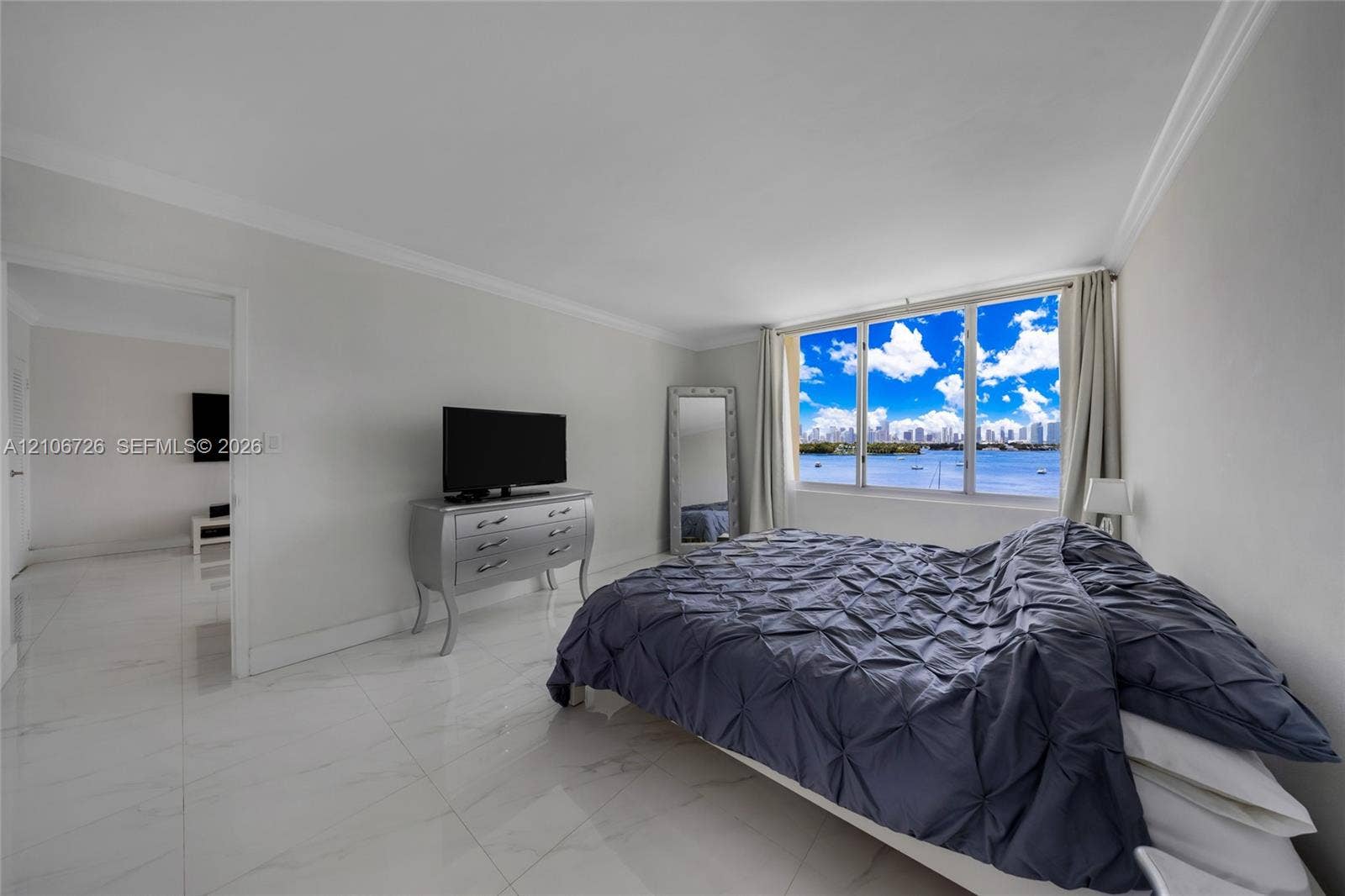 1200 West Avenue, #606, Miami Beach, Miami Beach, FL 33139 Interior space featuring polished white stone-finish flooring, crown molding, and expansive windows showcasing a water and skyline backdrop