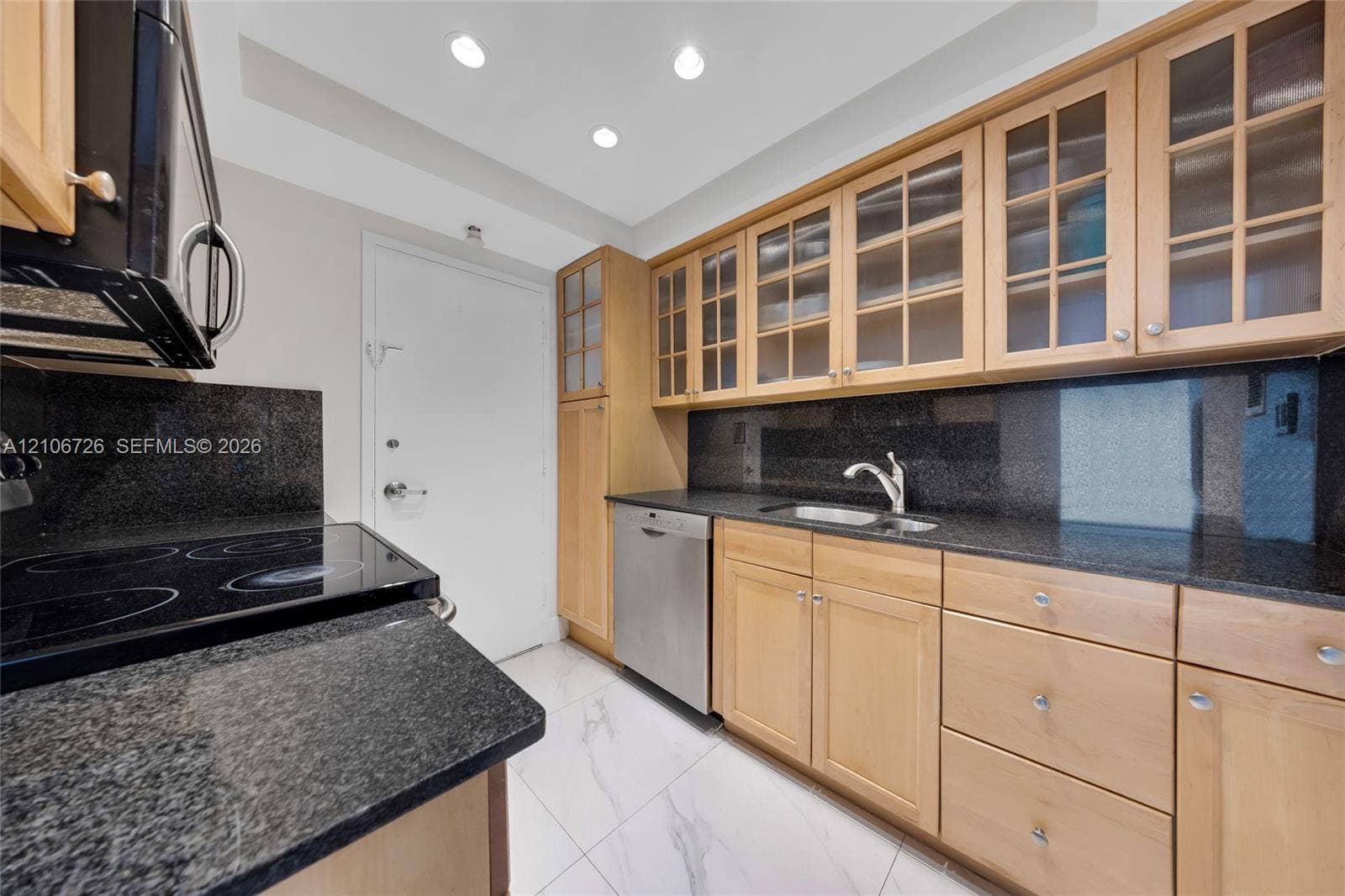 1200 West Avenue, #606, Miami Beach, Miami Beach, FL 33139 Kitchen featuring light wood cabinetry with glass-front upper doors, dark stone countertops, stainless steel dishwasher, integrated sink with gooseneck faucet, and white stone-finish flooring