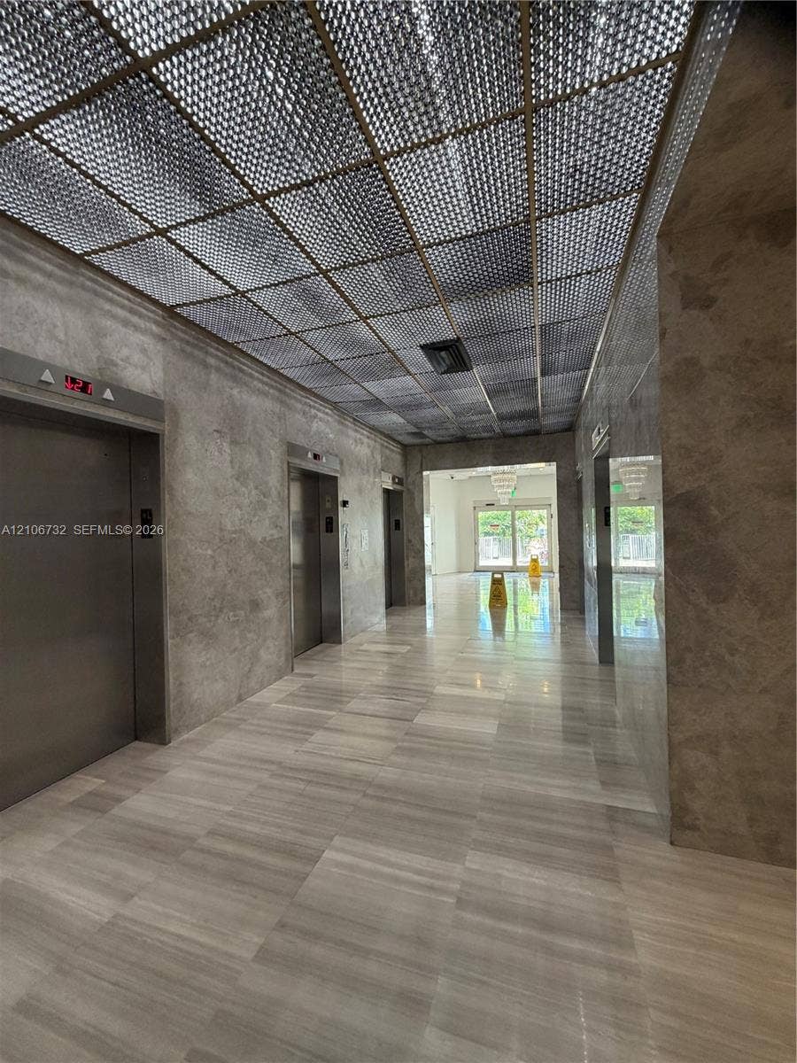 Lobby featuring stone wall cladding, polished stone flooring, grid-pattern ceiling detailing, and stainless steel elevator doors