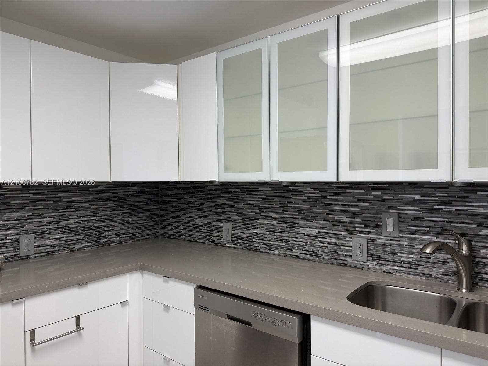 Contemporary kitchen featuring high-gloss white cabinetry, frosted glass cabinet inserts, solid-surface countertops, a linear mosaic tile backsplash, and an undermount stainless steel sink