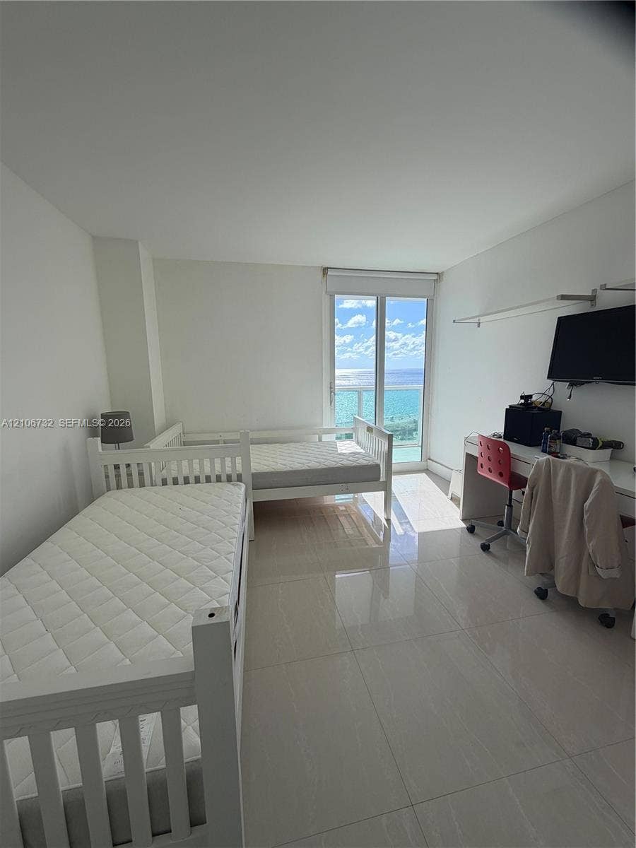 Room featuring polished tile flooring, floor-to-ceiling glass door, and balcony access with ocean backdrop