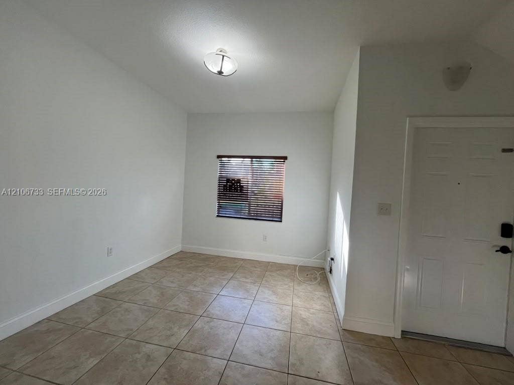Neutral-toned tile flooring, recessed window with horizontal blinds, overhead dome lighting, and white paneled entry door
