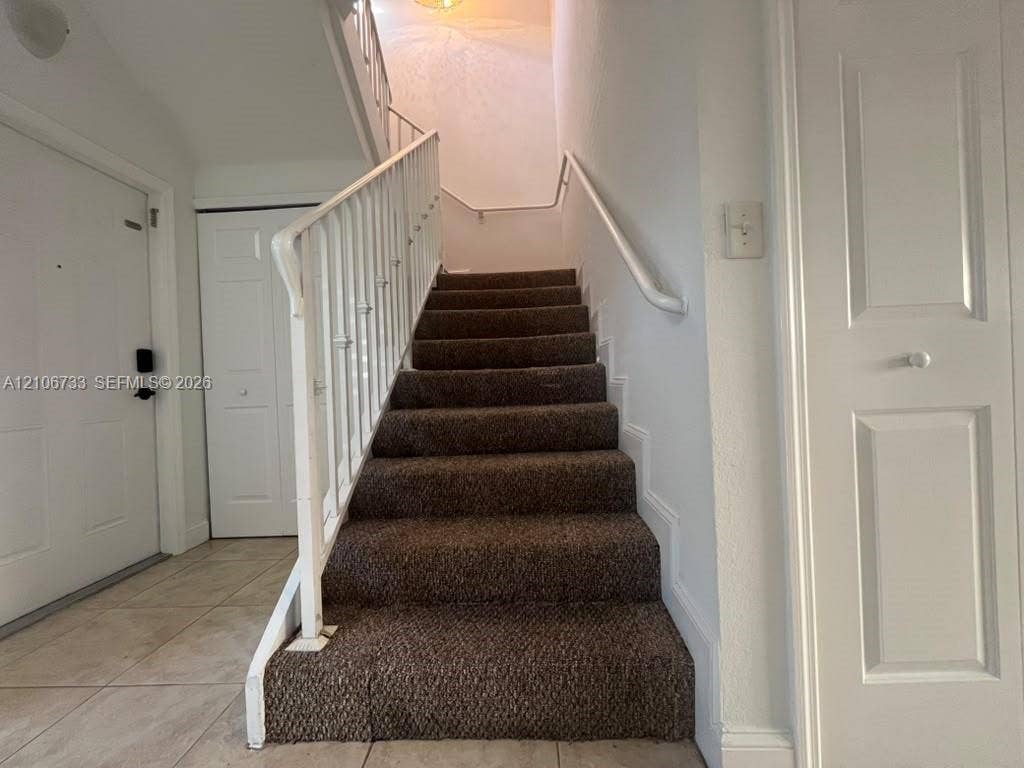 Entryway featuring tile flooring, staircase with carpeted treads, metal railings, and dual-panel interior doors