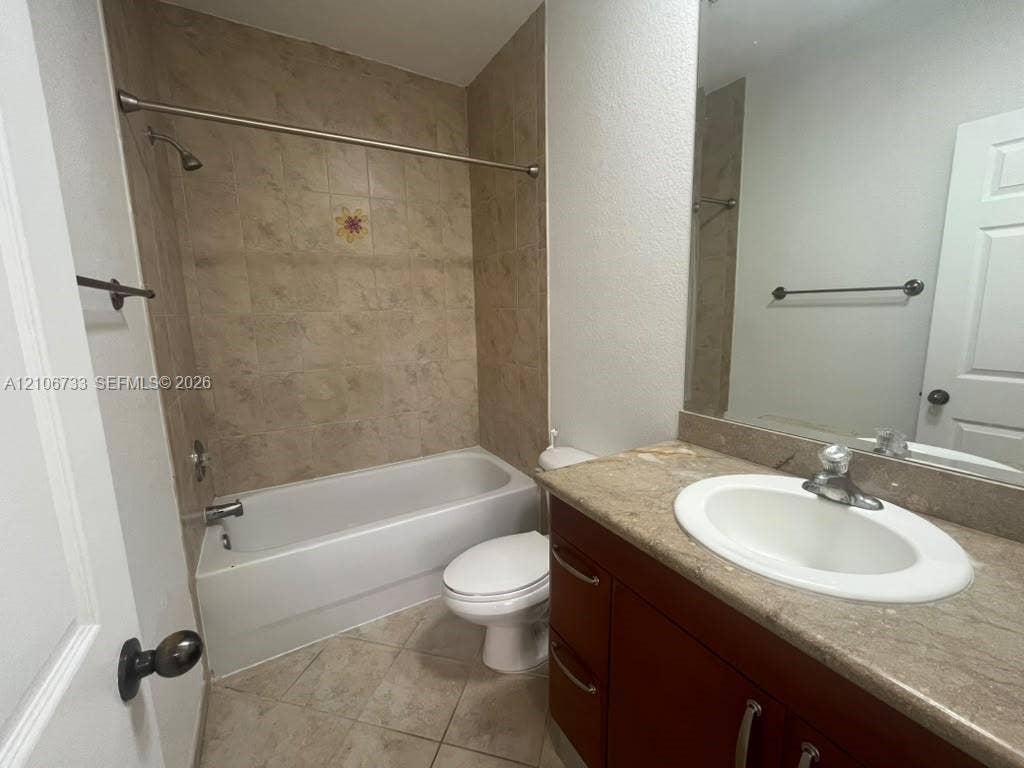 Bathroom featuring a vanity with a stone-finish countertop, undermount sink, shower-tub combination with tile surround, and tile flooring