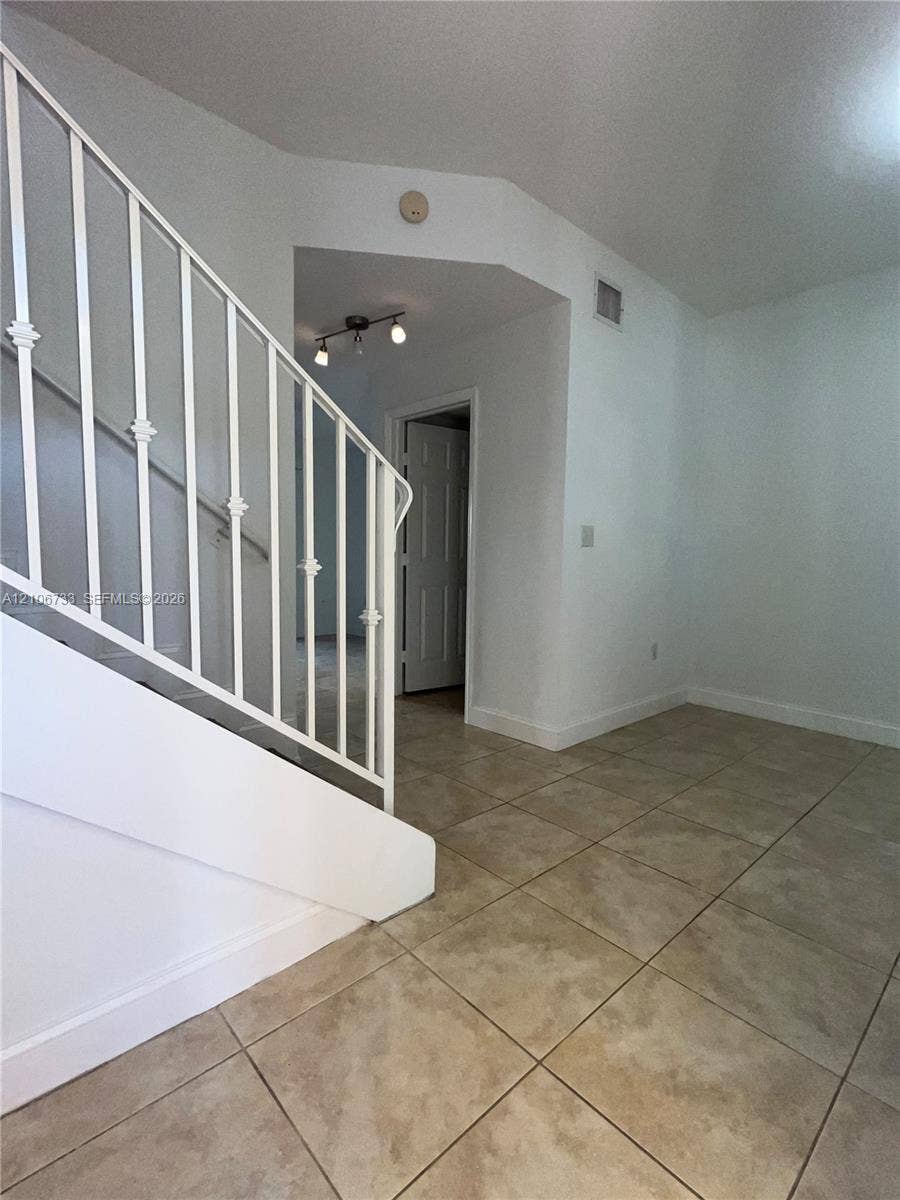 Staircase featuring white metal balusters, ceramic tile flooring, and multi-light ceiling-mounted fixture