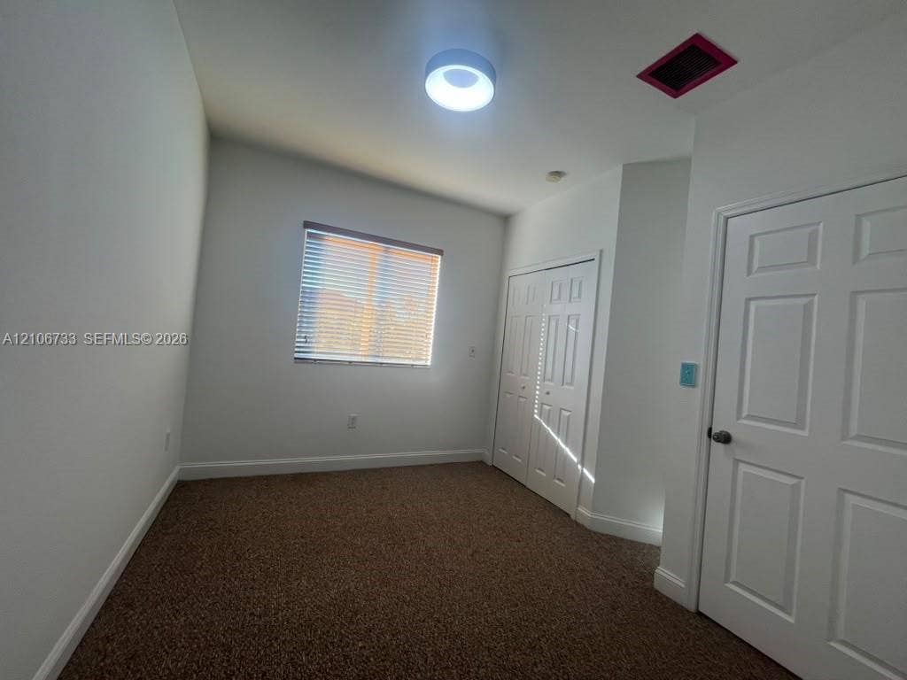 Room featuring neutral wall tones, carpeted flooring, a flush-mount circular light fixture, and double-panel closet doors