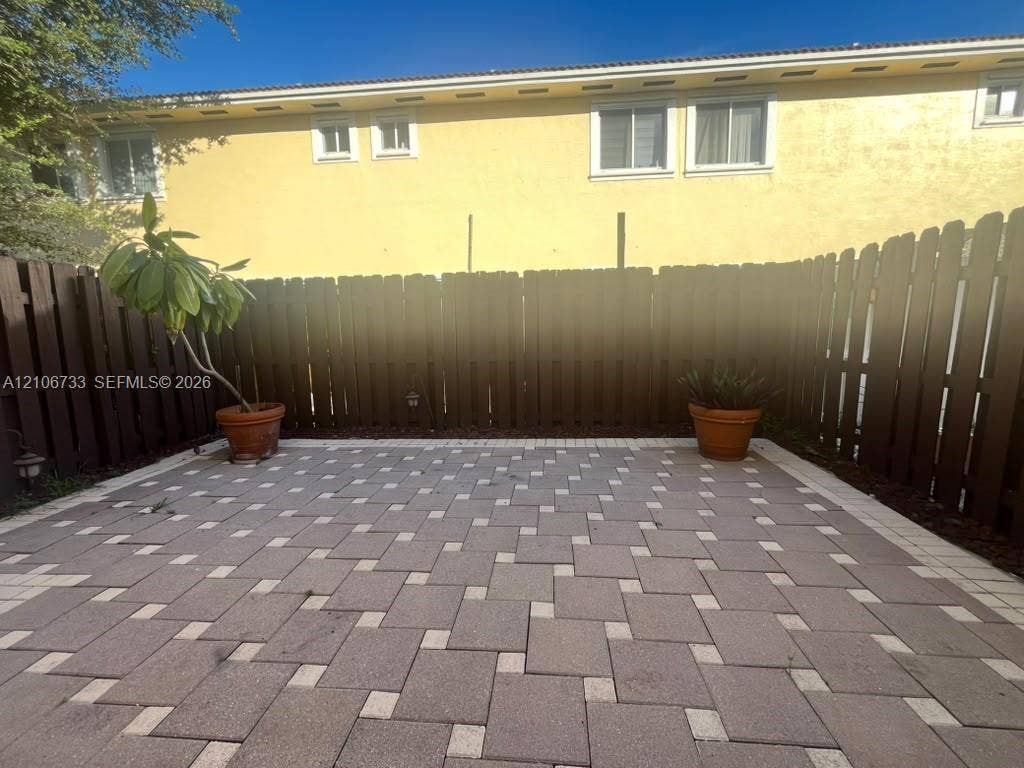 Enclosed patio featuring patterned stone pavers and a tall wooden privacy fence