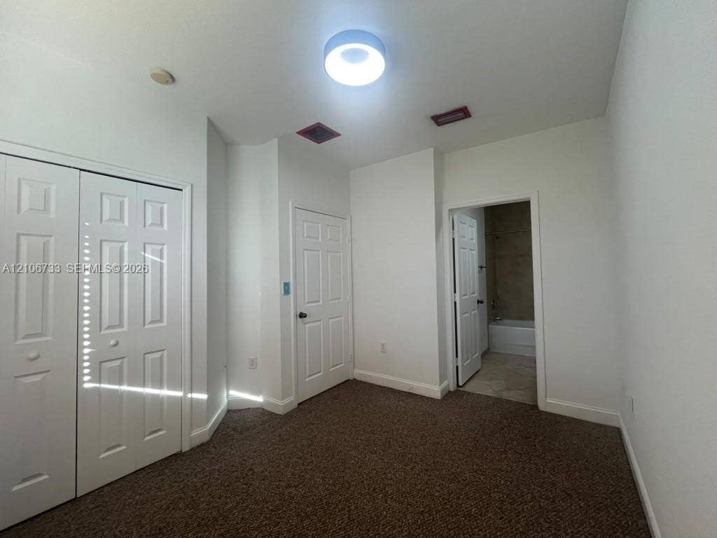 Room featuring wall-to-wall carpeting, dual-panel closet doors, single-panel interior doors, and a ceiling-mounted flush-mount light fixture
