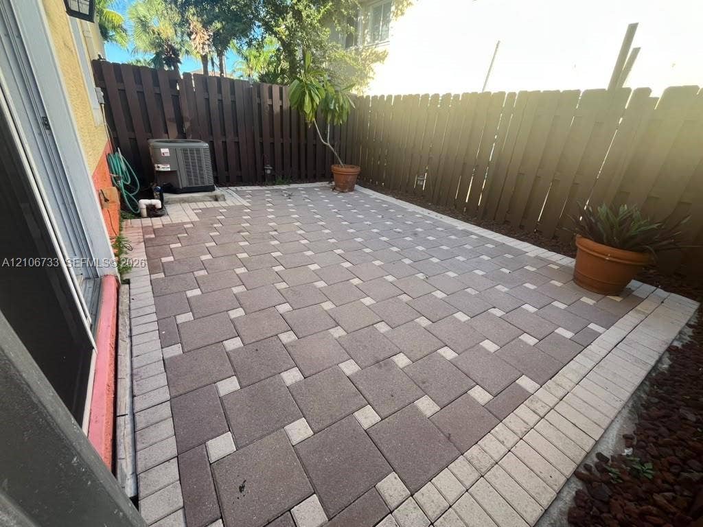 Private outdoor patio featuring interlocking concrete pavers, a decorative border, and a perimeter privacy fence